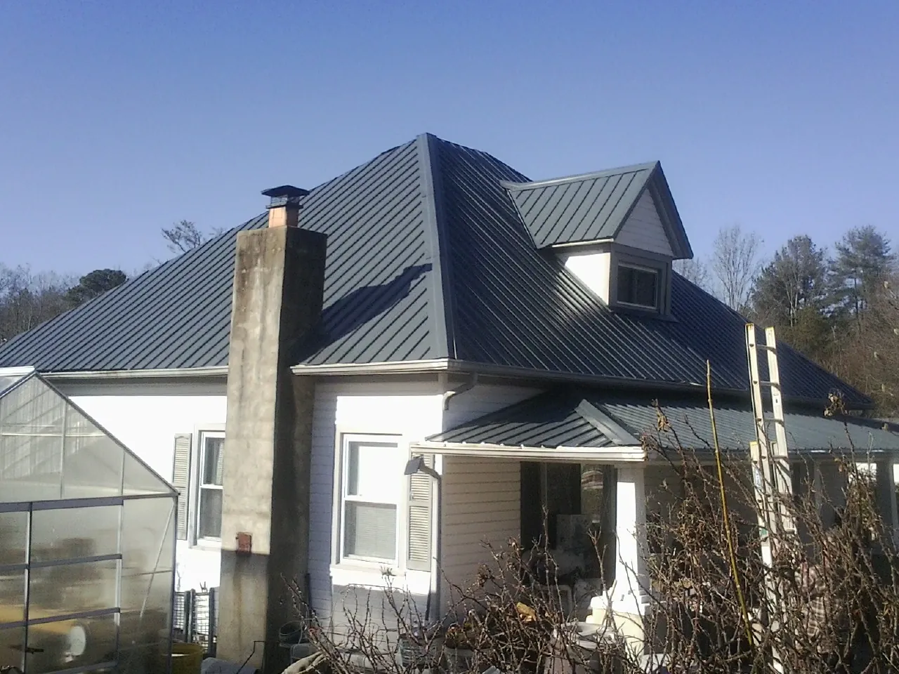Dark blue standing seam metal roof on a white farmhouse with dormer — Slate & Tile Roof Repair by Roofing Brothers in Arverne