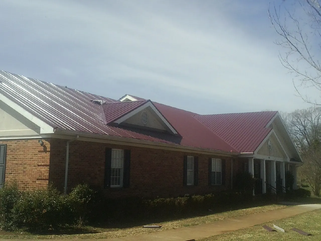 Red metal roof with gabled entries on a long brick building, from a Hail Damage Roof Repair job in Arverne