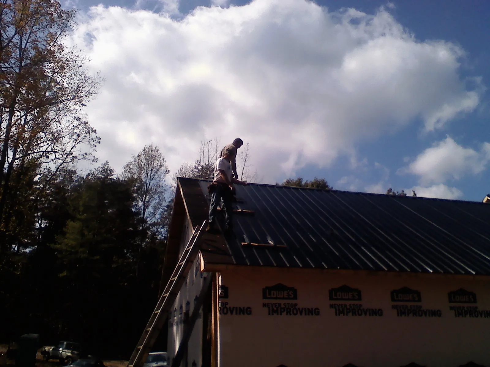 Roofer fastening dark metal panels high against a cloudy sky, from a Roof Inspection job in Arverne
