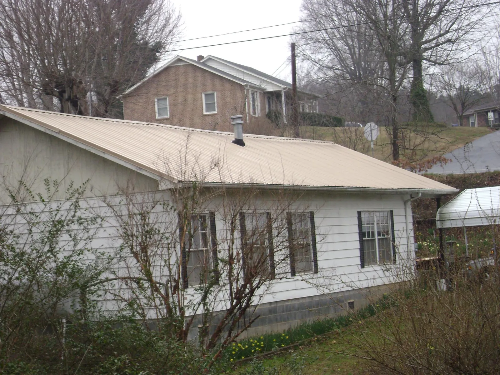 Tan metal roof on a white sided house set into a hillside — Commercial Roofing by Roofing Brothers in Arverne
