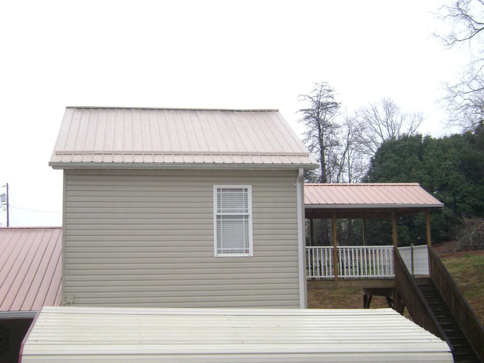 Tan metal roofs on a two story addition and attached porch, from a Roof Replacement job in Arverne